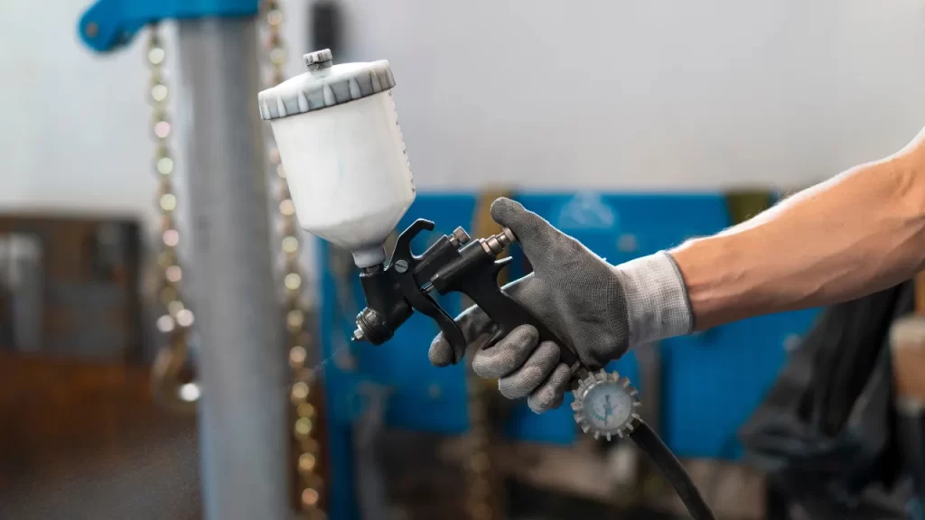 Mão de profissional utilizando pistola de pintura industrial com compressor de ar.