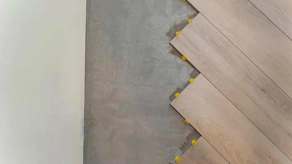 Instalação de piso cerâmico em padrão diagonal com espaçadores amarelos sobre contrapiso de concreto.